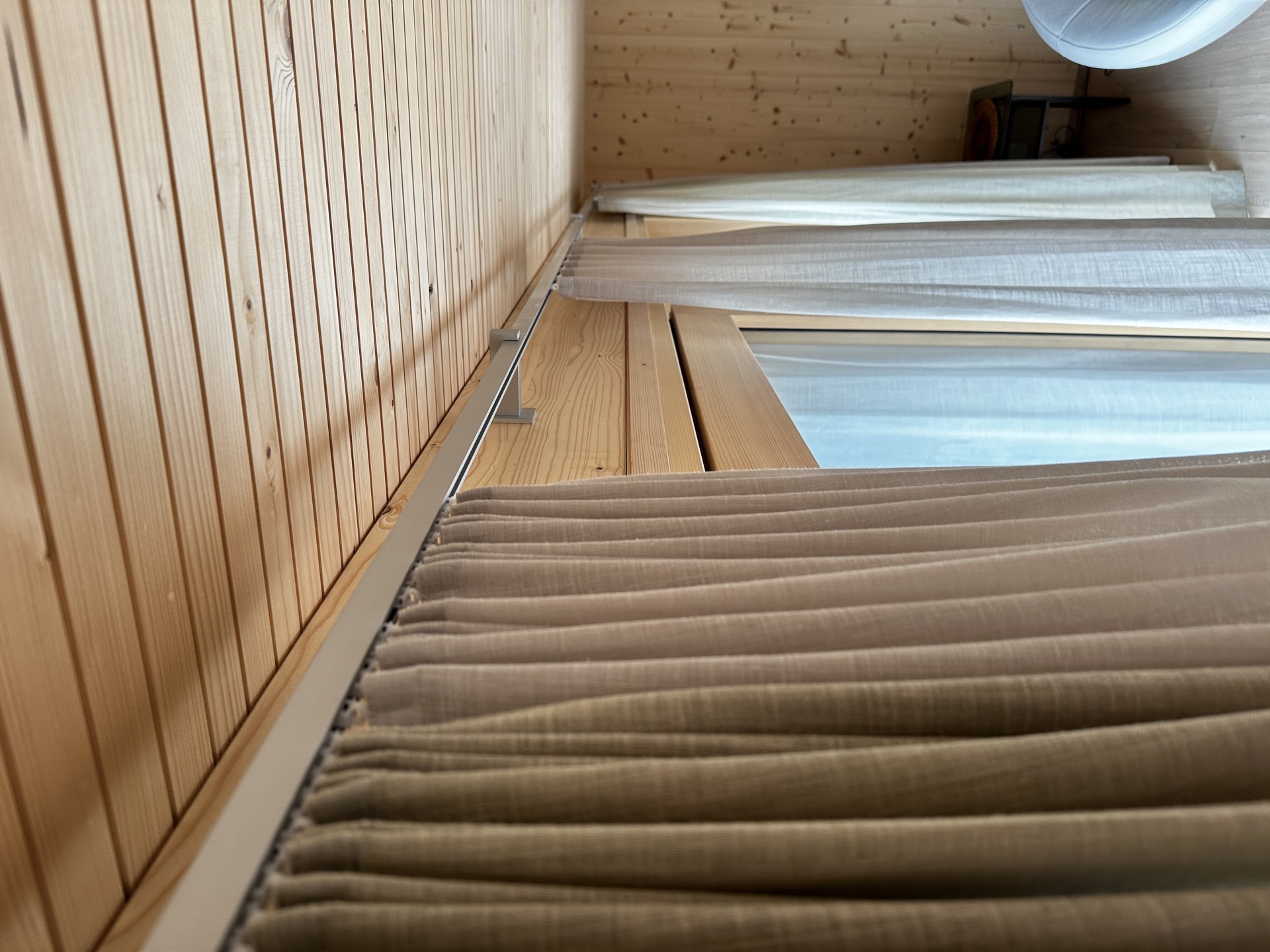 Blickdichter Dekovorhang und transparenter Tagesvorhang an deckenmontierter Schiene im Holzchalet